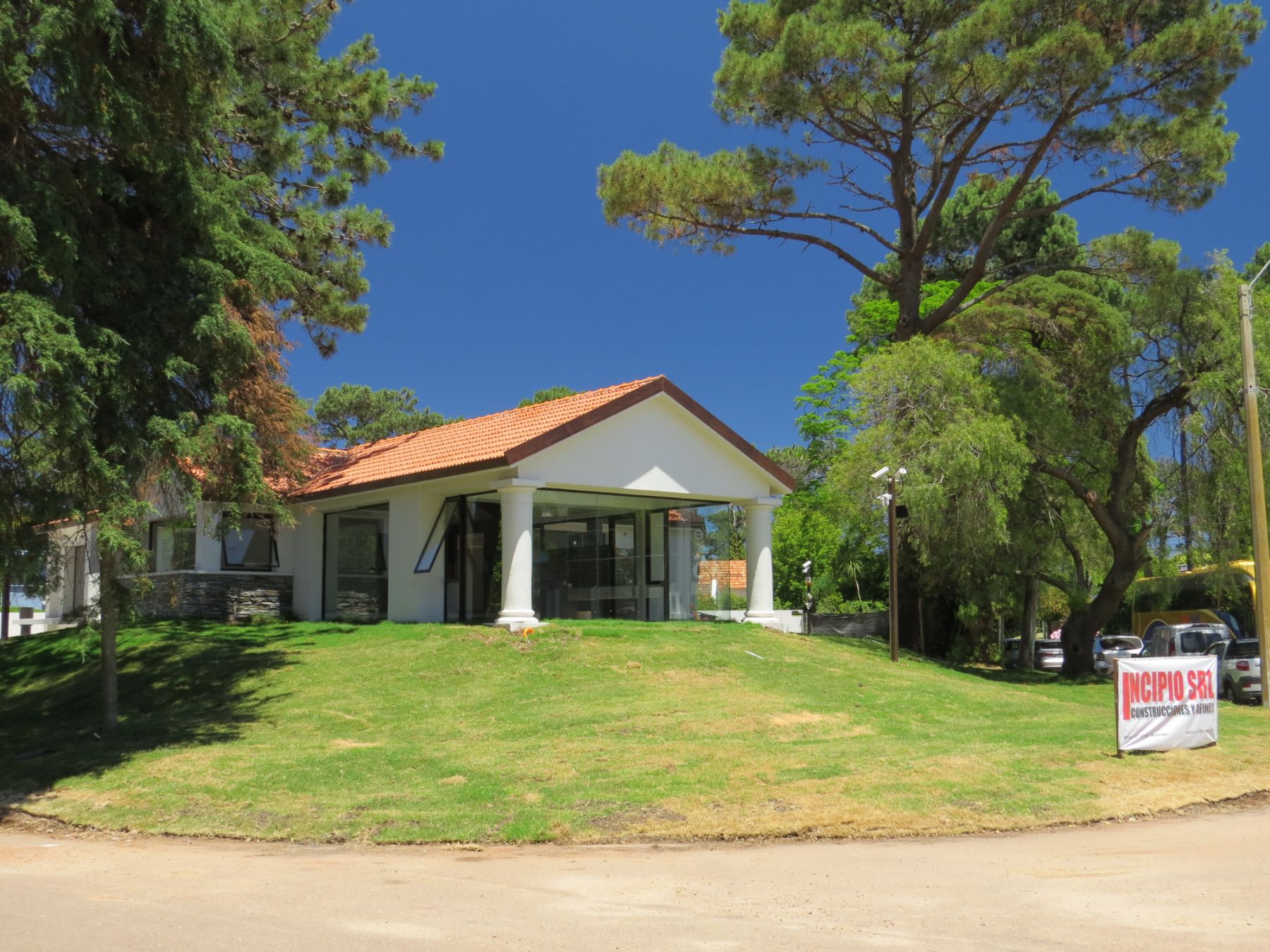 Imágen en la que se ve la construcción de la clínica terminada, enfocada desde la proa en la que se ve el tejado a dos aguas, apoyado sobre dos columnas redondas que enmarcan un ventanal grande. Todo esto sobre una pequeña colina en cuya base se encuentra el cartel de Incipio SRL.